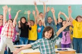 Niños de la escuela con los brazos en alto en un aula, celebrando con sonrisas.