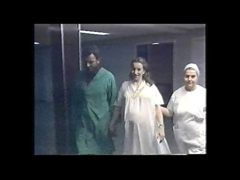 Un hombre, una mujer embarazada y una enfermera caminan por un pasillo de hospital.
