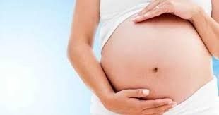 Mujer embarazada sosteniendo su vientre, piel clara, top blanco, fondo azul.