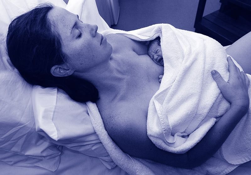 Una nueva madre acuna a su recién nacido, envuelto en una toalla, en una cama de hospital.