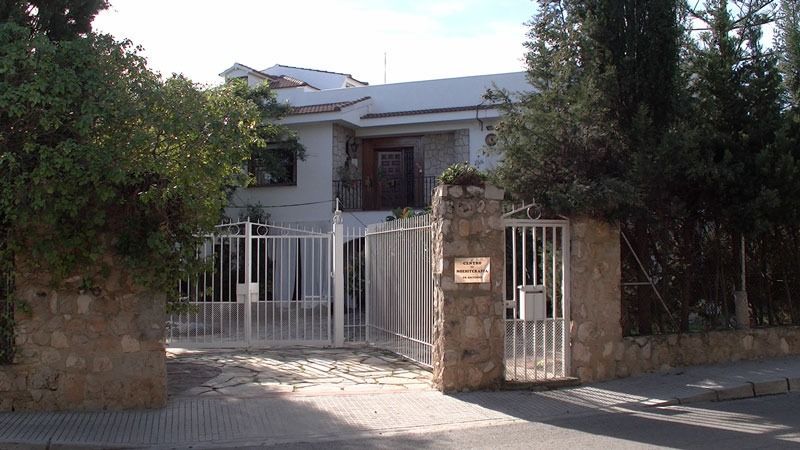 Casa blanca detrás de una entrada cerrada con columnas de piedra y árboles a ambos lados.