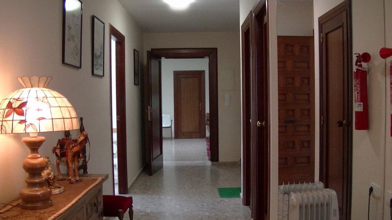 Pasillo con puertas abiertas, paredes beige y una lámpara de mesa a la izquierda.