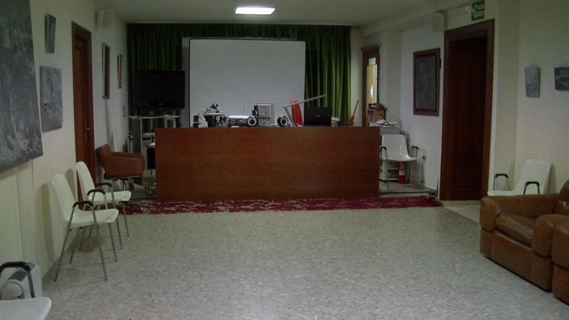 Una oficina con un escritorio grande, sillas, pantalla de proyección y una sala de espera.