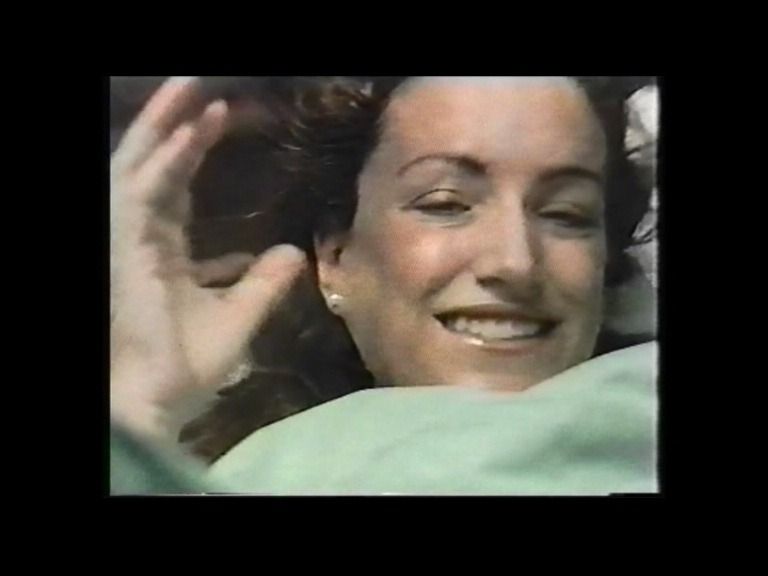 Mujer sonriendo, cabeza y hombros, mano levantada, acostada, manta verde pálido.