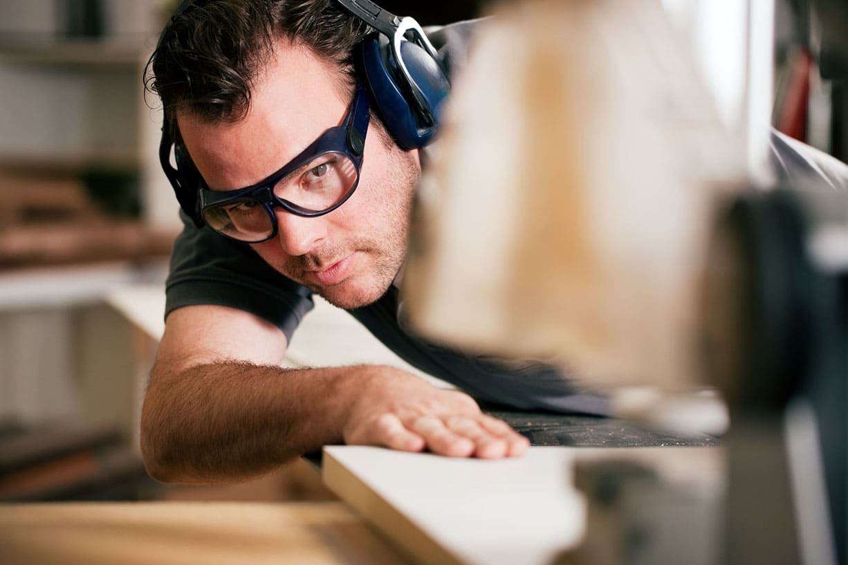 Un homme portant un casque antibruit et des lunettes de sécurité ponce une surface en bois dans un atelier.