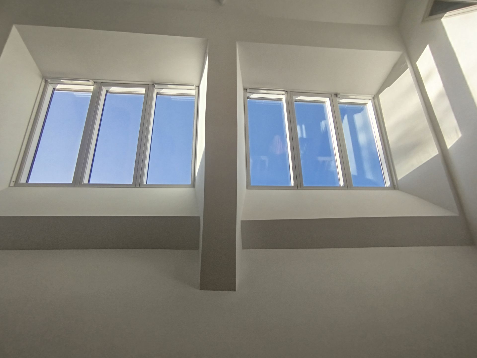 Deux fenêtres de toit à cadre blanc, laissant apparaître le ciel bleu, séparées par un pilier blanc.