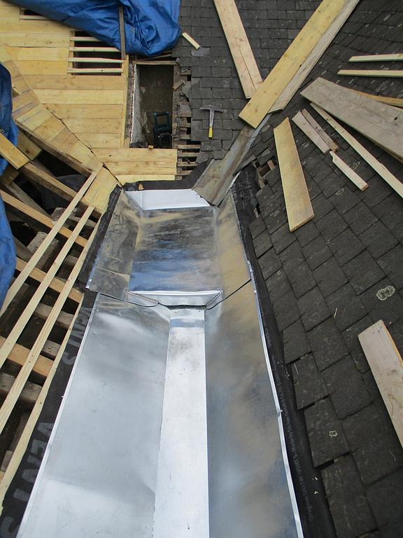 Solin de noue métallique nouvellement installé sur un toit, entouré d'une charpente en bois et de bardeaux.