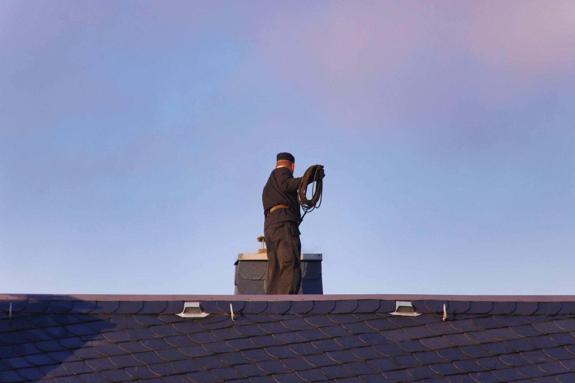 ramonage-cheminée Homme debout sur un toit qui ramone une cheminée