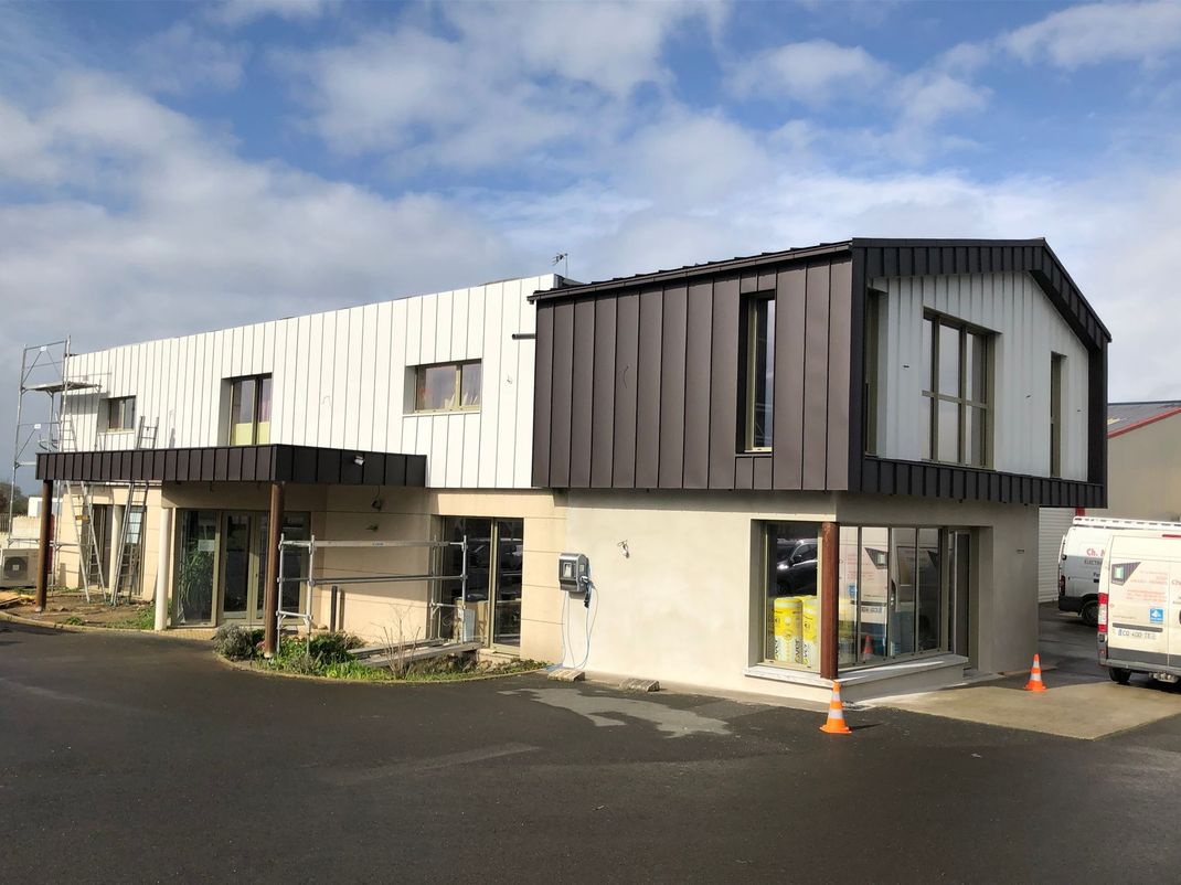 Extérieur du bâtiment, deux étages, bardage en zinc et aluminium. Échafaudages visibles. Ciel nuageux.