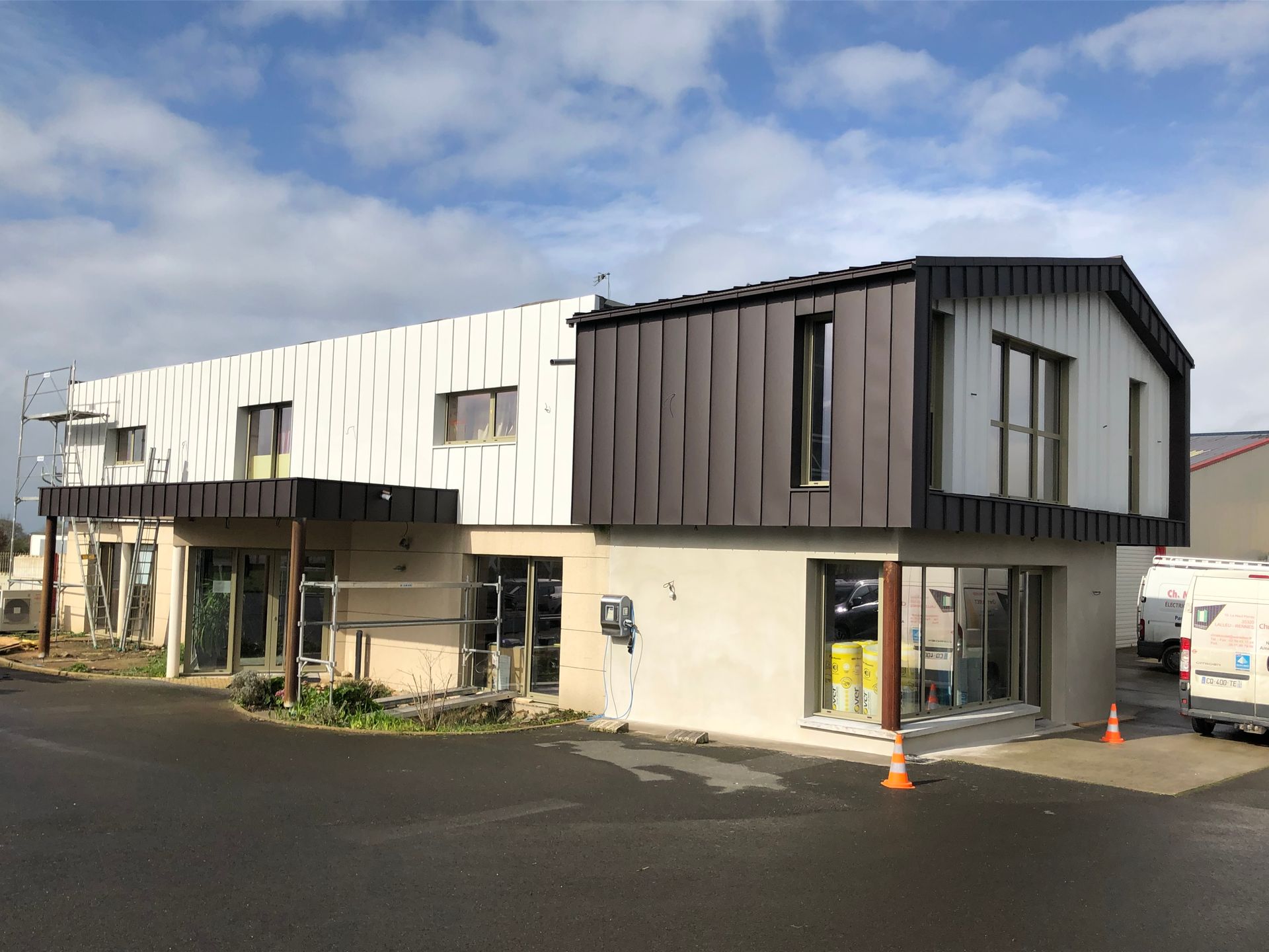 bardage-zinc-aluminium Extérieur du bâtiment, deux étages, bardage en zinc et aluminium. Échafaudages visibles. Ciel nuageux.