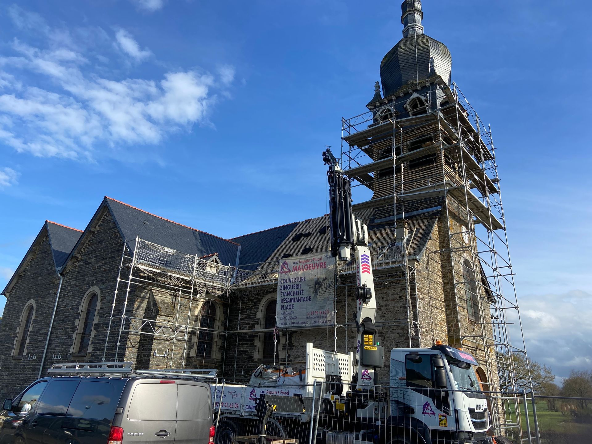 L'église est en rénovation ; des échafaudages entourent le clocher et une nacelle élévatrice se trouve à proximité.