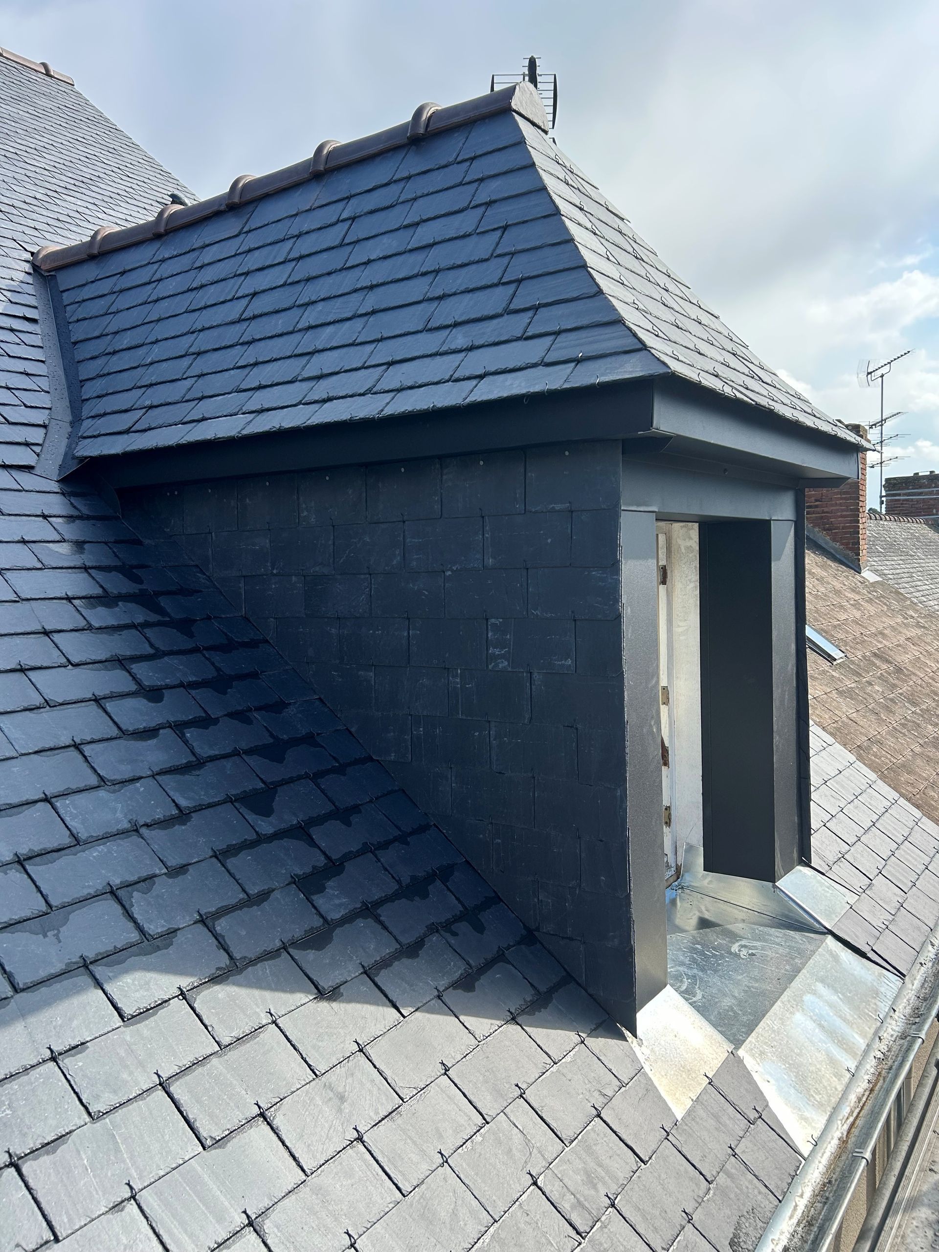 Toit en ardoise avec lucarne. Mur en briques avec encadrement de fenêtre.