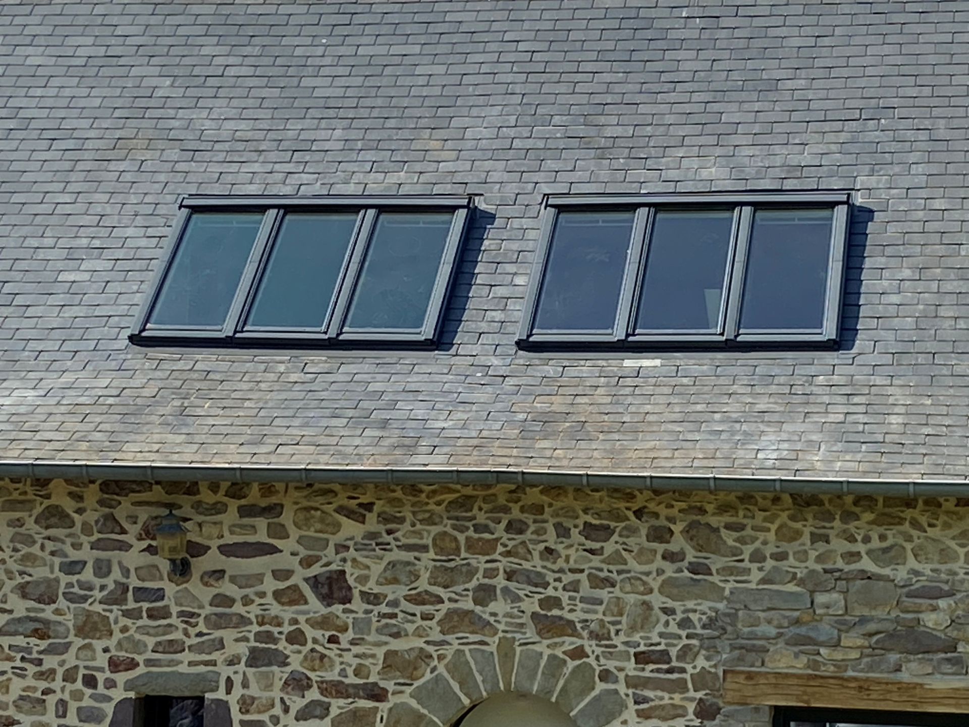 Toit en ardoise avec deux fenêtres de toit au-dessus d'un mur en pierre.