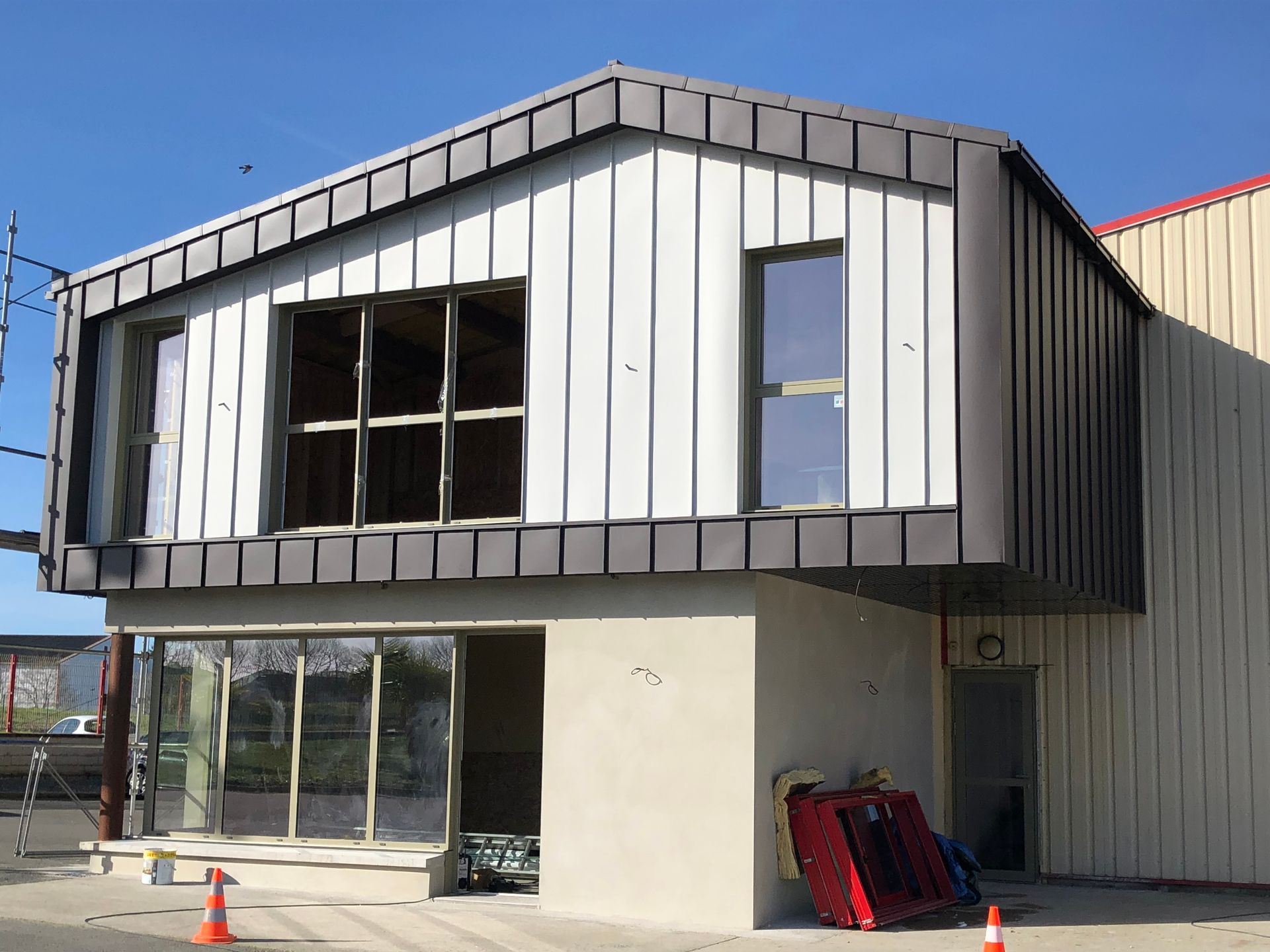 Extérieur du bâtiment, structure à deux étages en construction ; bardage en zinc et aluminium.