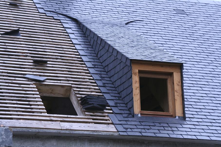Toiture partiellement recouverte de bardeaux avec une lucarne, laissant apparaître des ardoises neuves.