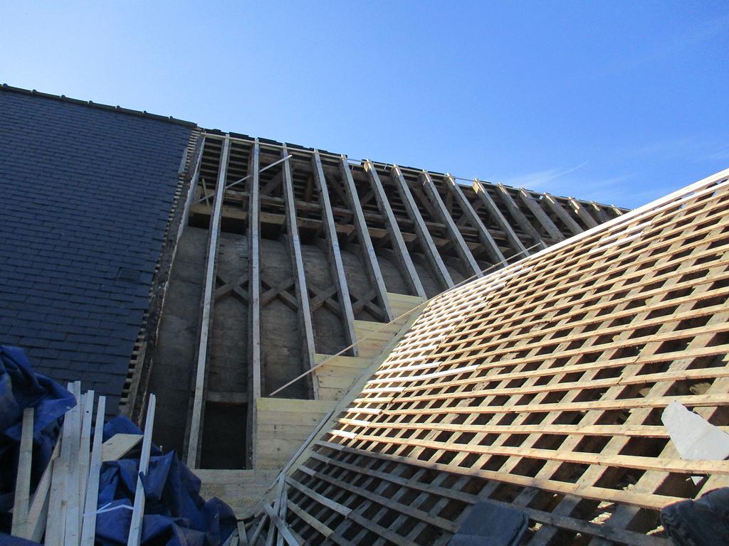 Toiture en construction, avec chevrons et charpente en bois apparents, sur fond de ciel bleu.