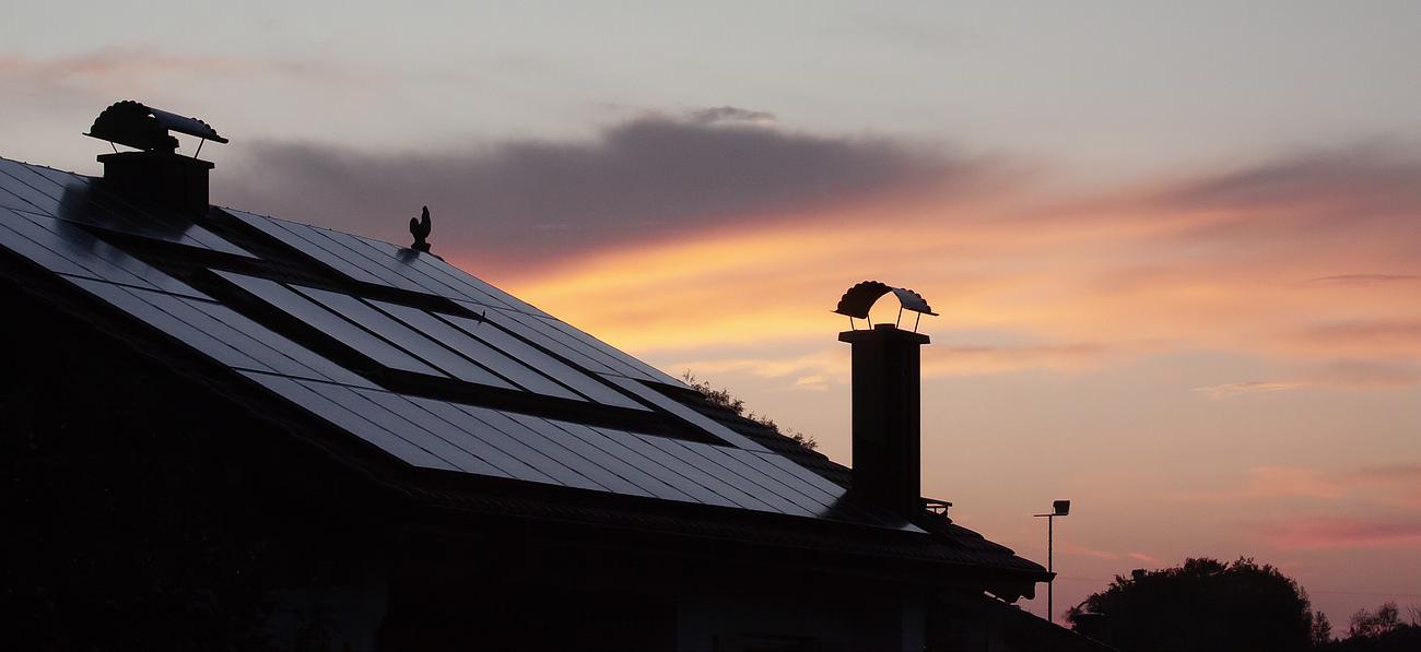 Toit de maison en silhouette avec cheminées se détachant sur un ciel de coucher de soleil aux couleurs chatoyantes.