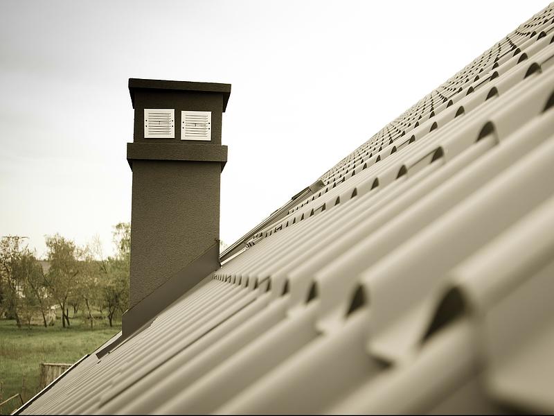 Toiture métallique grise avec cheminée, se détachant sur un ciel nuageux et des arbres en arrière-plan.