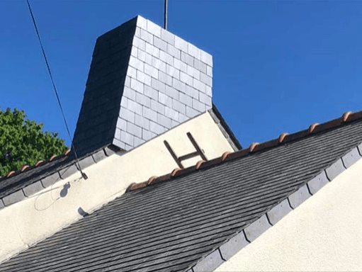 Cheminée en ardoise sur un toit de bardeaux gris foncé, sous un ciel bleu.