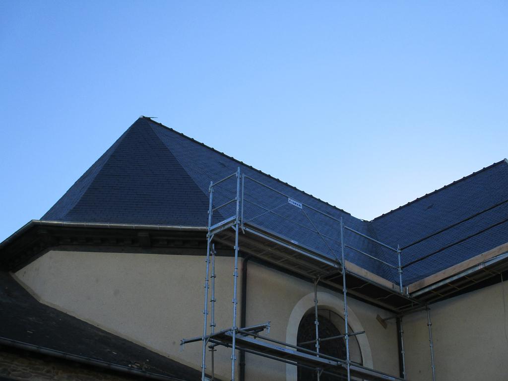 Toit d'ardoise sombre sur un bâtiment clair, avec des échafaudages visibles.