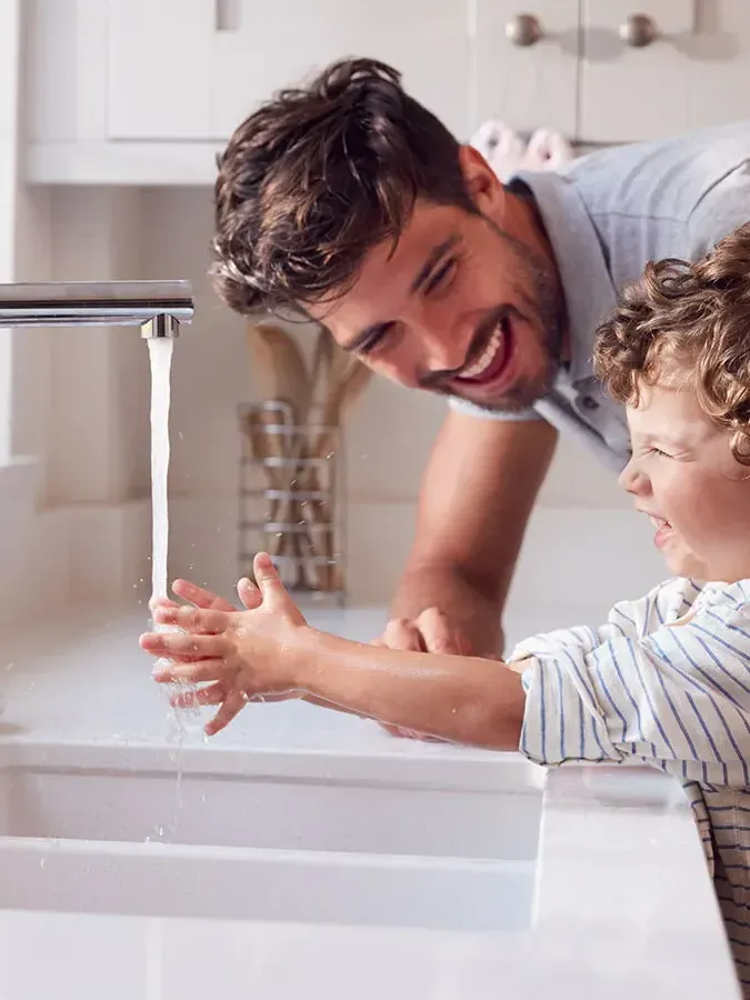 Un enfant qui se lave les mains en rigolant avec son père