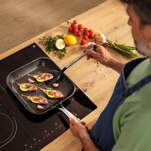 Persona que utiliza una batidora de mano para batir crema en un recipiente de vidrio sobre una superficie de madera.