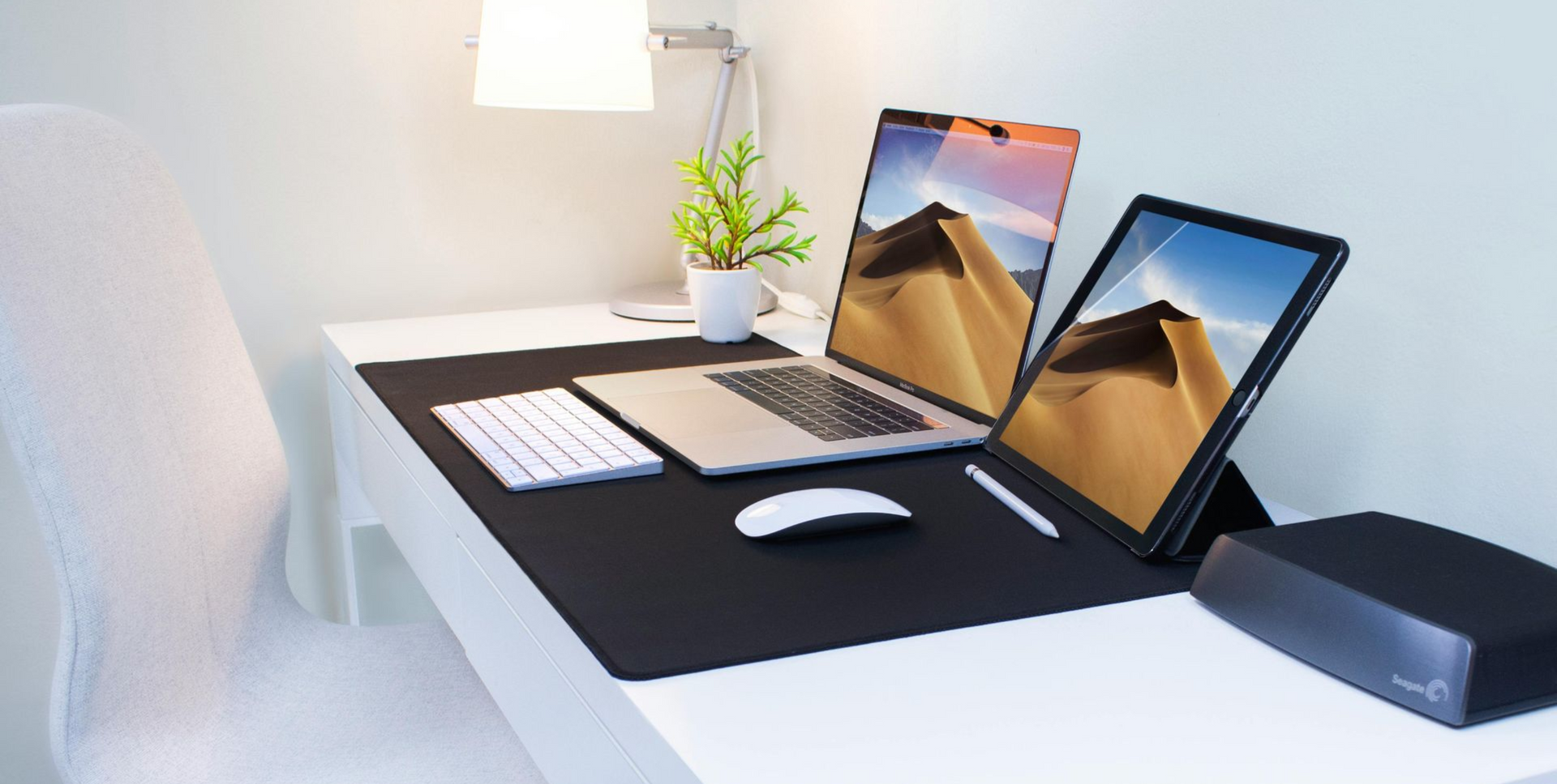 Un escritorio blanco con una computadora portátil, una tableta, un teclado, un mouse, un lápiz y un disco duro externo.