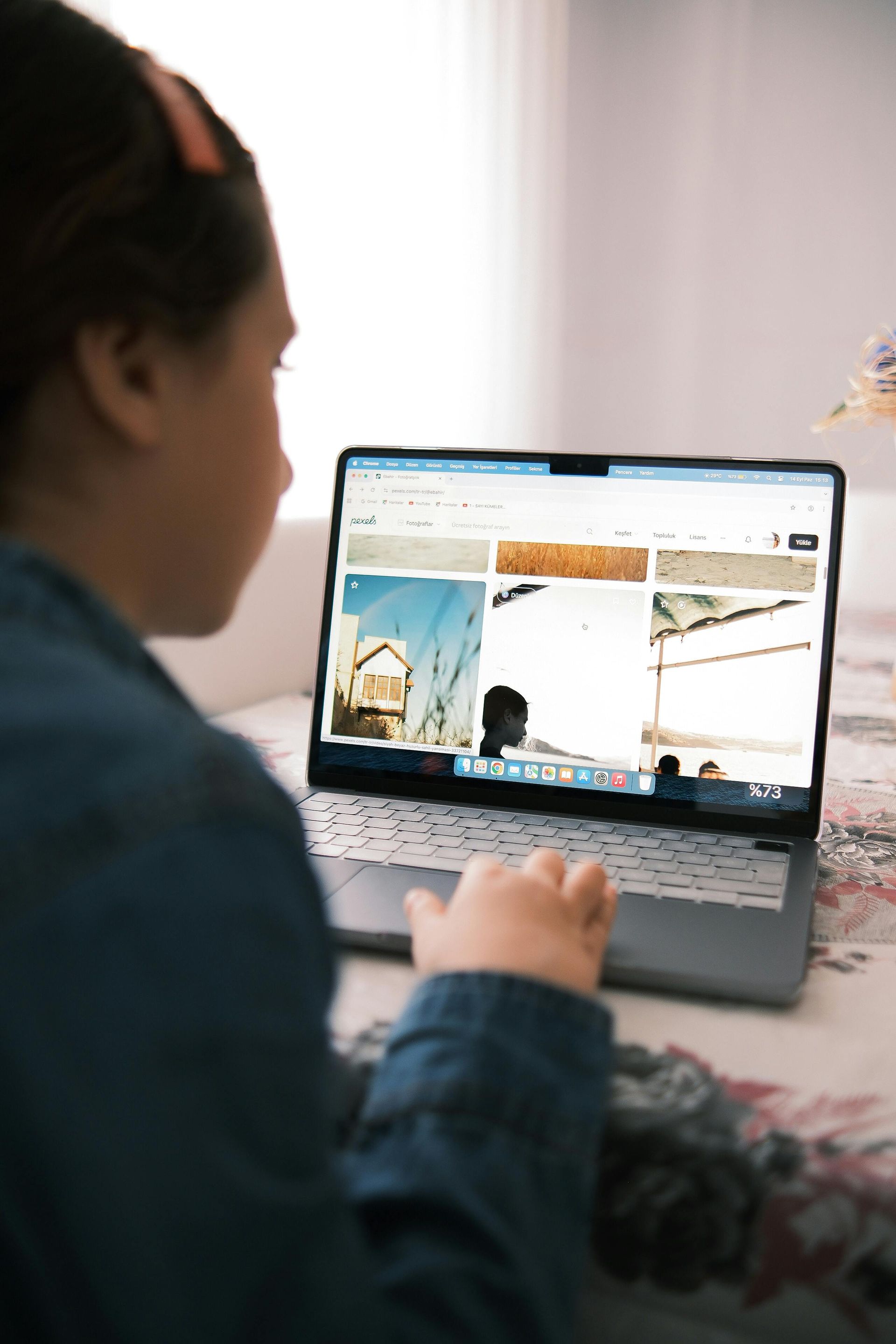 Chica usando una computadora portátil, mirando fotos; en el interior, en una cama, vistiendo jeans azules.