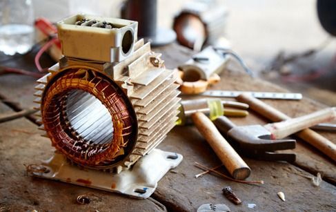Primer plano de una bobina de motor de cobre con herramientas esparcidas sobre un banco de trabajo