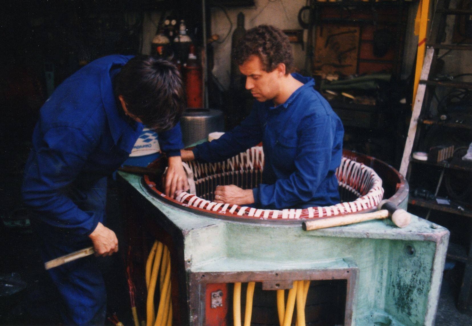 Dos personas con chaquetas azules trabajando en un objeto circular a rayas en un taller