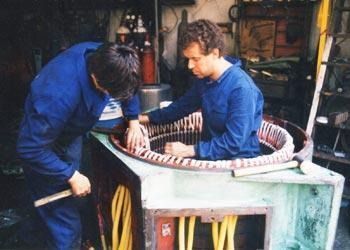 Dos trabajadores con camisetas azules reparan una gran máquina cilíndrica en un taller.