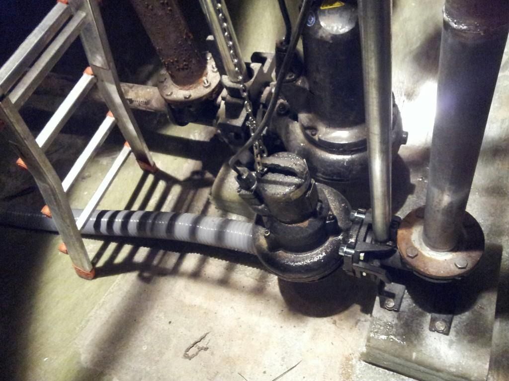 Tuberías y válvulas industriales, con tuberías aisladas de color negro junto a la barandilla metálica de una escalera en un sótano oscuro