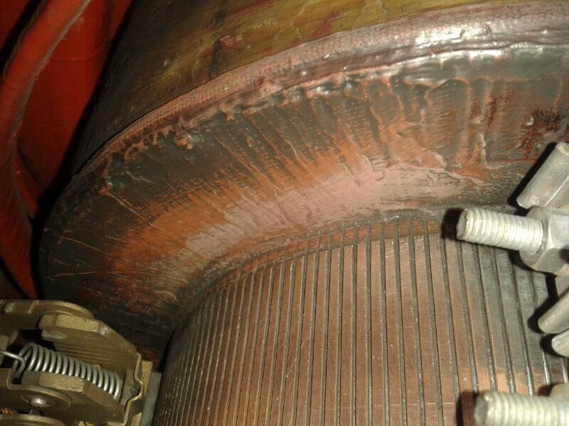 Primer plano de una unión de tubería metálica oxidada con un accesorio roscado blanco y la superficie corroída.