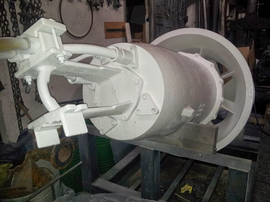 Gran máquina cilíndrica blanca montada sobre una estructura metálica en un taller, con brazos mecánicos acoplados.
