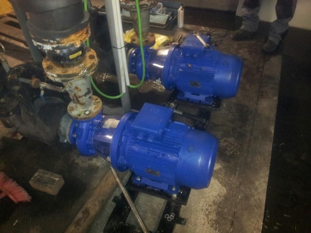 Dos bombas industriales azules conectadas a tuberías sobre el suelo mojado de una fábrica