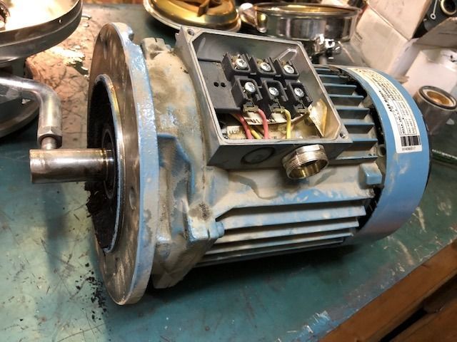 Motor eléctrico desmontado sobre un banco de trabajo, con el cableado a la vista y la carcasa metálica
