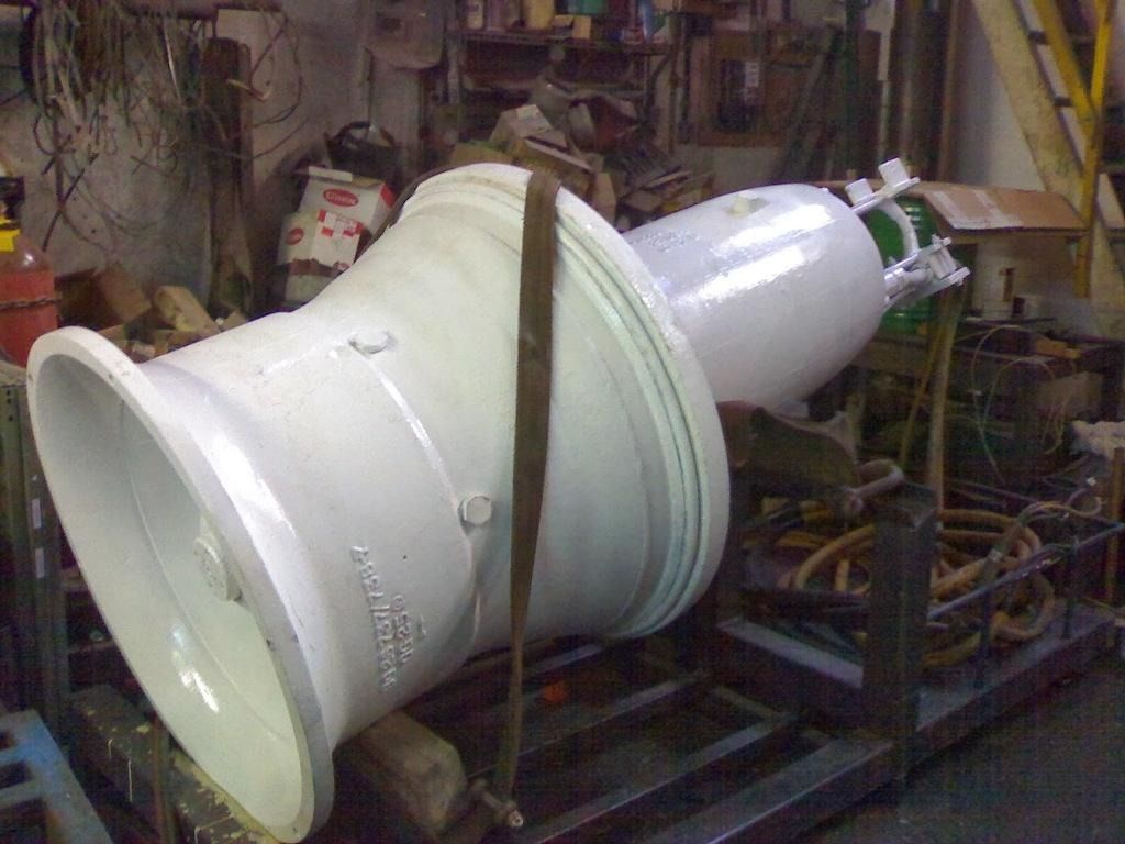 Pieza blanca de una máquina industrial montada sobre una estructura metálica en un taller, con mangueras y equipos a su alrededor