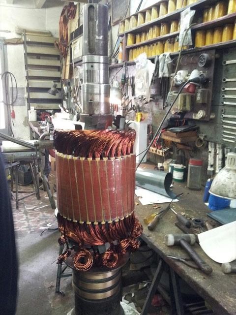 Armadura de un gran motor eléctrico con los bobinados de cobre al descubierto en un taller, rodeada de herramientas y estanterías