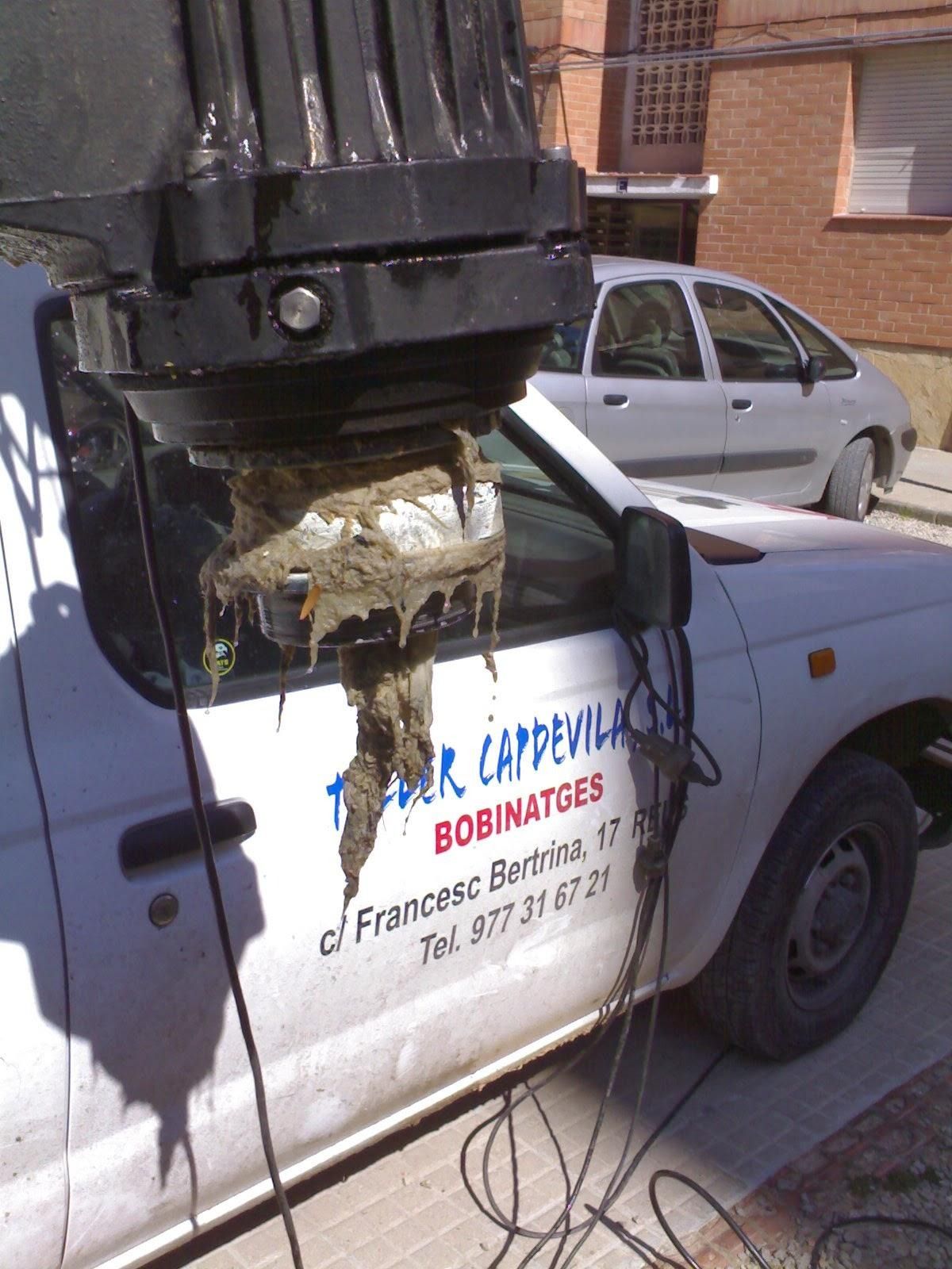 Un poste de servicios públicos dañado sobre una furgoneta blanca, con cables colgando sobre el capó, en una calle de la ciudad