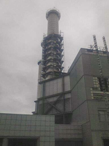 Industriegebäude mit hohem Schornstein an einem bewölkten Tag.