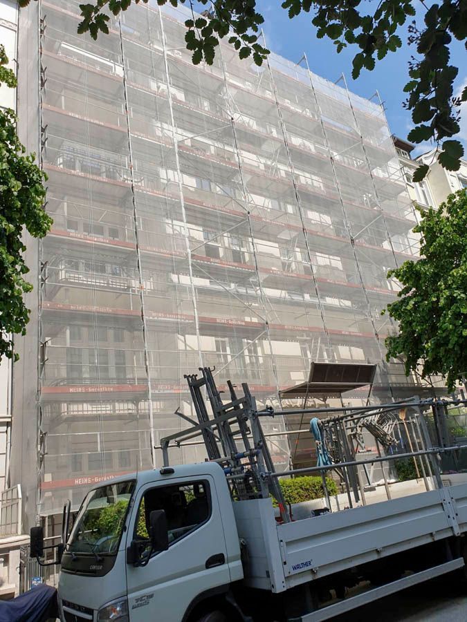 Die Gebäudefassade ist mit Gerüsten und Netzen verhüllt, davor steht ein Lastwagen.