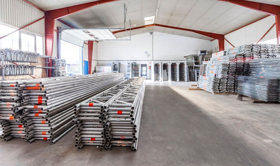 Das Innere der Lagerhalle war mit gestapelten Metallgerüsten und roten Stützbalken gefüllt.