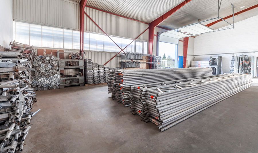 Innenansicht einer Lagerhalle mit gestapelten Metallgerüstbauteilen.