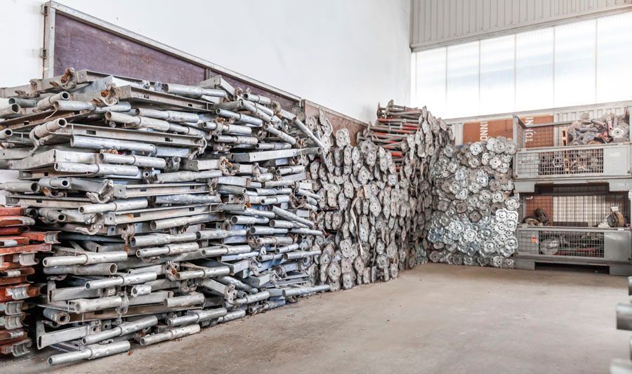 Gerüstteile wurden in einer Lagerhalle gelagert. Metallkonstruktionen waren aufgestapelt, grau und silberfarben.