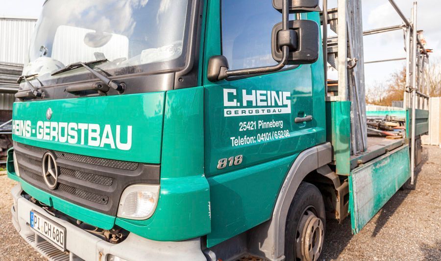 Grüner Mercedes-Lkw mit dem Logo „C. Heing Gerustbau“ und Kontaktinformationen parkt im Freien.
