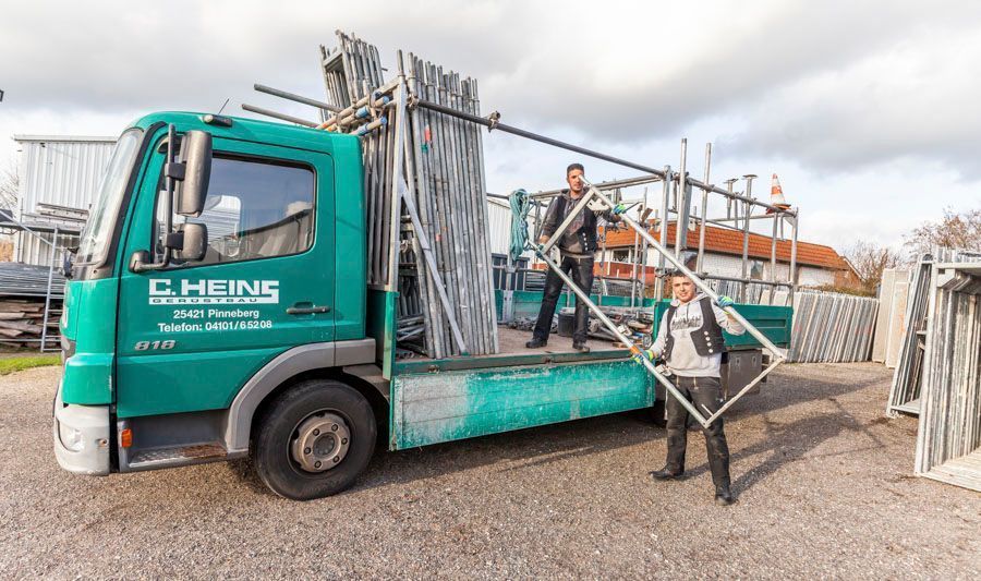 Grüner Lastwagen mit zwei Personen, die an einer Baustelle Fensterrahmen halten.