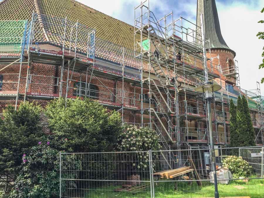 Gebäude mit Gerüst, im Bau. Rote Backsteinfassade, grünes Dach und ein hoher Turm.