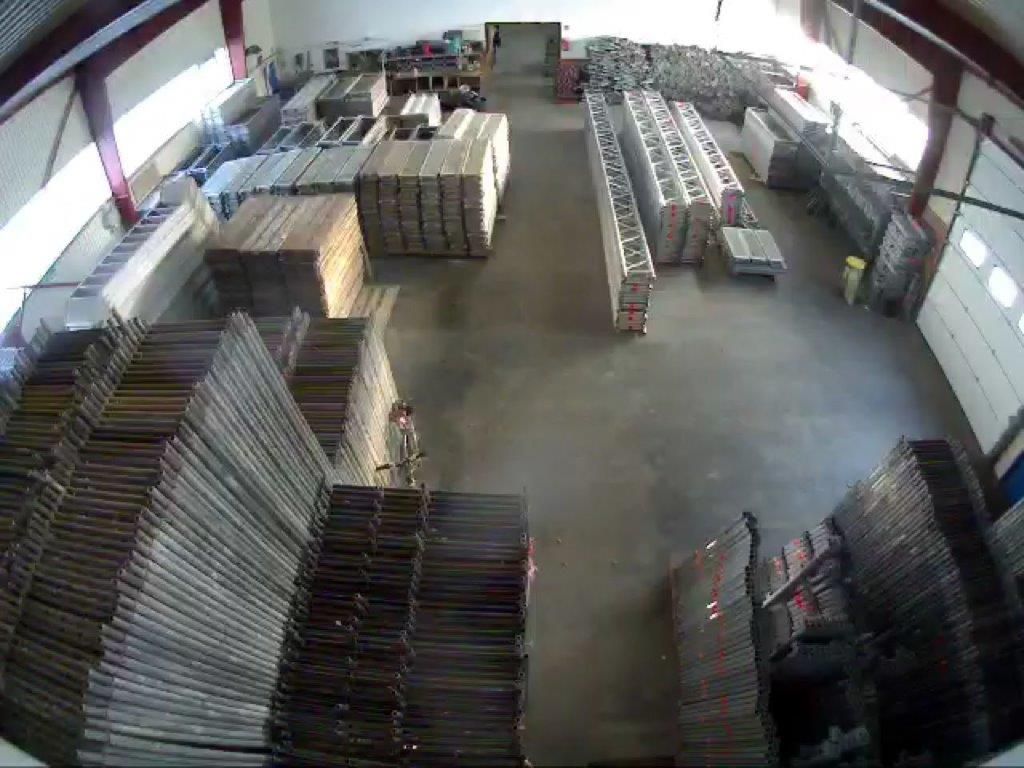 Innenansicht einer Lagerhalle mit gestapelten Materialien und Ausrüstungsgegenständen, vermutlich für Bauzwecke, von oben betrachtet.