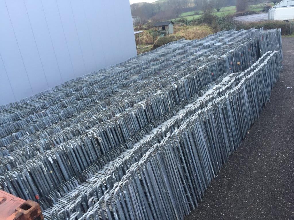 Stapel von Metallzaunpaneelen auf Asphalt, in der Nähe eines Gebäudes.