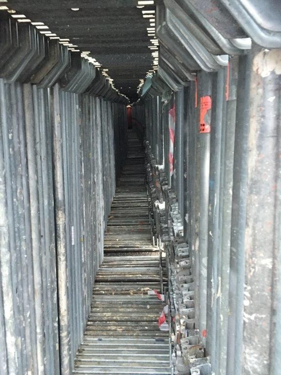 Blick in einen schmalen, dunklen Korridor, der von schwarzen Gerüsten gesäumt ist.